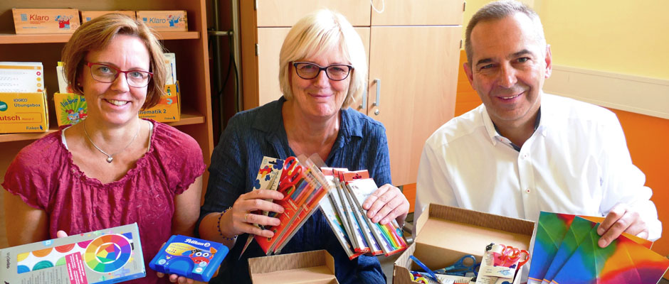 Ansgar Montag von der Caritas übergibt Material an Claudia Huhmann-Rohkämper (stellvertretende Leiterin) und an Monika Müller (Leiterin) von der Grundschule Kunterbunt.